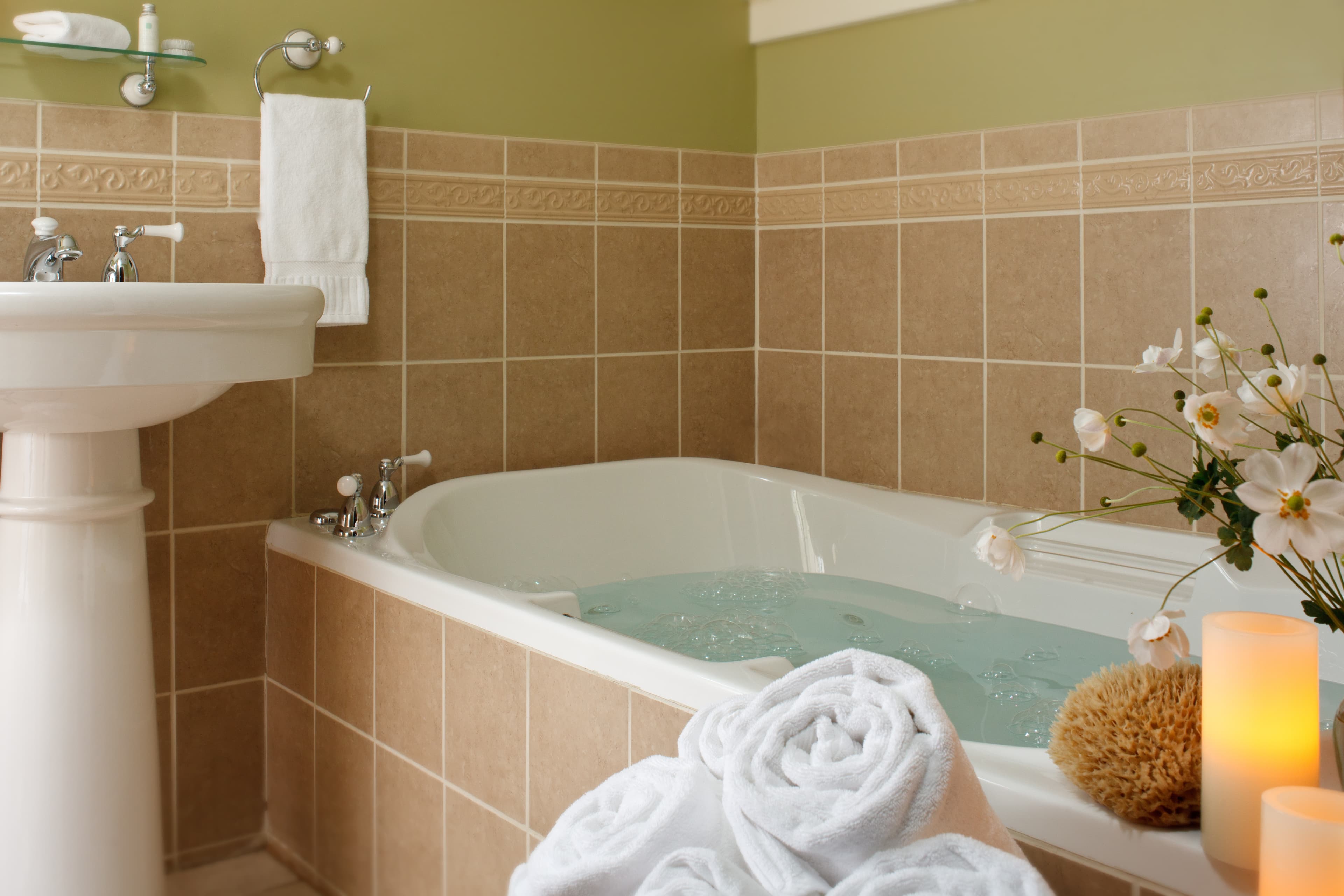 A serene bathroom setup with a filled bathtub, lit candles, towels, and flowers.