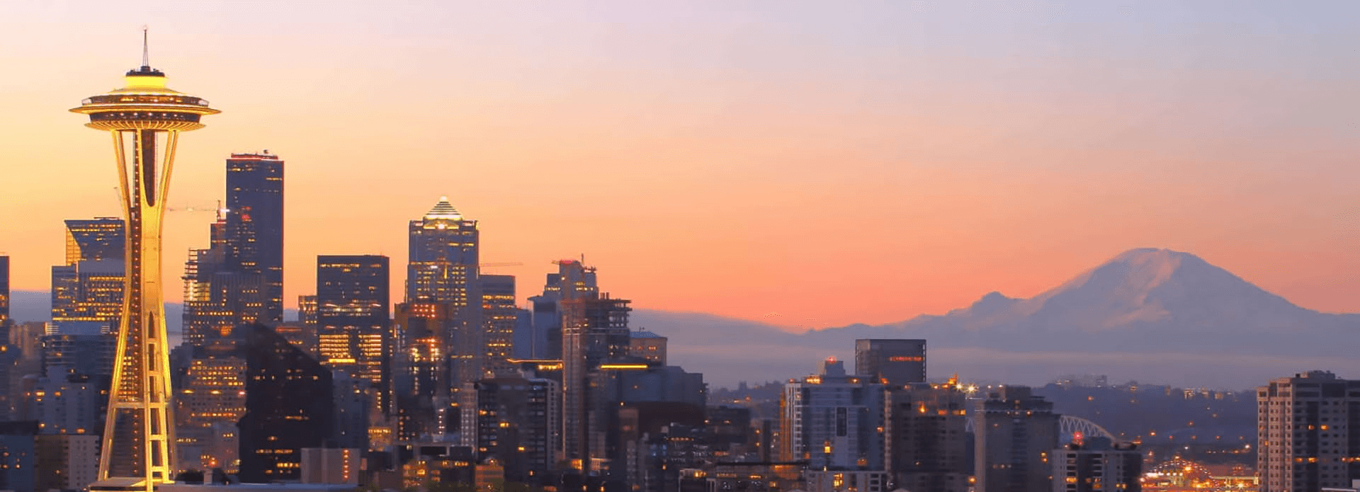 Seattle skyline at sunset featuring the Space Needle and Mount Rainier in the background.