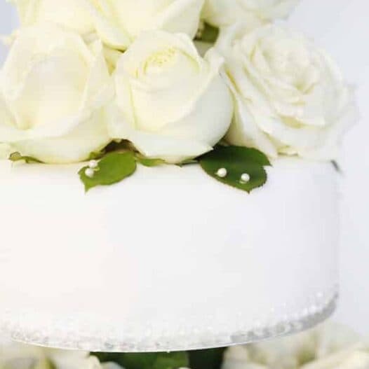 A white cake topped with white roses and green leaves.